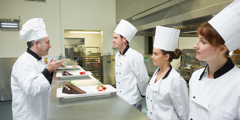 A culinary class where a pastry chef lecturer is teaching his students in a professional kitchen